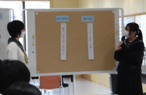 制服姿の女子高校生2人が、2つの俳句が貼りだされたホワイトボードの両脇に立ち、1人がマイクを持って話をしている様子の写真