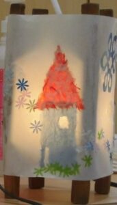 白い和紙に貼られた赤い屋根の家や花の模様が糸巻きの内側からの光で浮かび上がる手作り行灯の写真