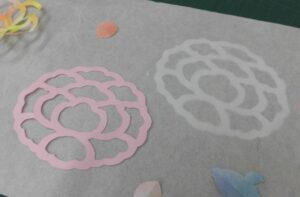 薄桃色と白の牡丹の形をした切り絵がなどが和紙の上に並んでいる写真