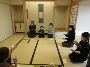 和室の畳の上に参加者が円座に座り茶碗を手に点前を味わいながら伝統的な作法を体験する茶道の場面の写真