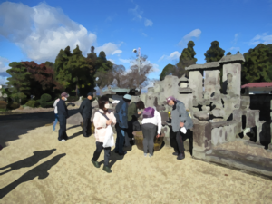 柔らかな質感で描かれた風景の中、複数の人々が墓石周囲で清掃作業を協力して進めている様子の写真