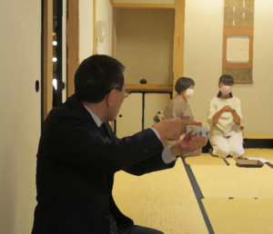 和室の畳の上で、スーツ姿の男性が香炉を両手で大切に持ちながら香の聞き方を学んでいる様子の写真