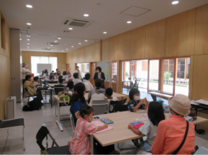 広い室内に並んだテーブルの席に参加者の子どもたちや保護者が座り、作業をしている様子の写真