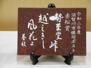 白い文字で赤松賞の俳句が刻まれた赤茶色の石板の写真