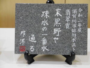 白い文字で翡翠賞の俳句が彫られた灰色の石板の写真