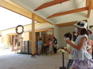 屋根付きの広いテラスで、子どもたちが天井から下がった丸い輪に向けて紙飛行機を投げて遊んでいる写真