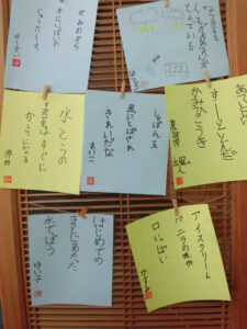 木製のクリップで木枠に留められて展示された、水色や緑の四角い紙に書かれた俳句作品が複数並んでいる写真