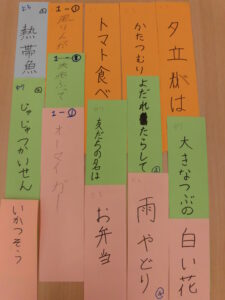 手書きの文字が書かれた、オレンジ、緑、ピンク、水色の短冊が、複数組み合わさって並べられている写真