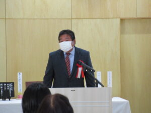 壇上でスーツ姿の人物がマイク前に立ち話をしている様子の写真