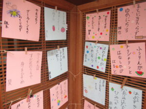 2枚続きの木製のパーティションに、俳句とイラストが描かれた水色やピンク色の四角い紙が整然と貼られ、展示されている写真