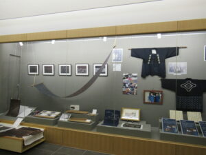 ガラスケース内に藍染の反物や写真資料、法被などが整然と並んでいる展示風景の写真