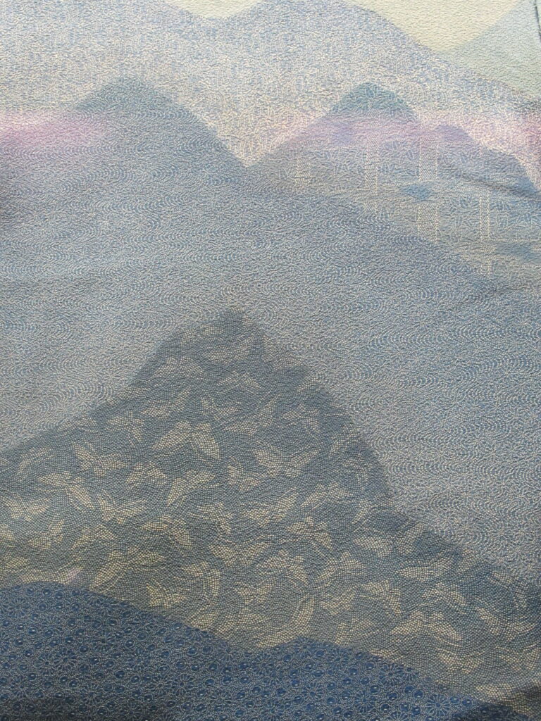 青の濃淡で重なる山並みに細かな文様が散りばめられた着物生地の精緻な柄を近距離で捉えた写真