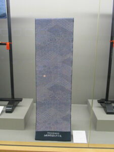 細かな文様が全体に施された青を基調とした反物が台座に立てて展示されている写真