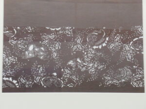 茶系の布地一面に白い花や葉のような模様が配置された生地のクローズアップ写真