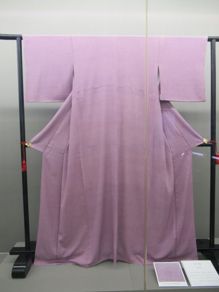 黒い衣桁にかけて展示された淡い紫色の無地の着物の写真
