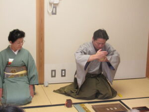 薄い緑色の着物の女性の隣に座った和装の男性が、香道の作法で香りをかいでいる様子の写真