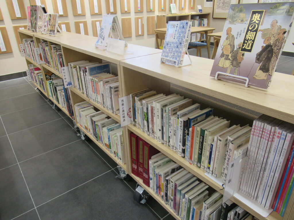 木製の低い書棚に多くの本が整然と並び、上段には数冊の本がスタンドで展示された図書貸出スペースの写真