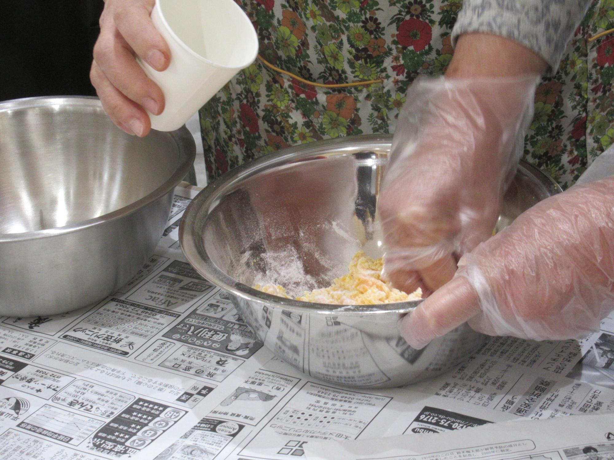 ビニール手袋をして、ステンレスのボウルの中の材料をこねている手元の写真