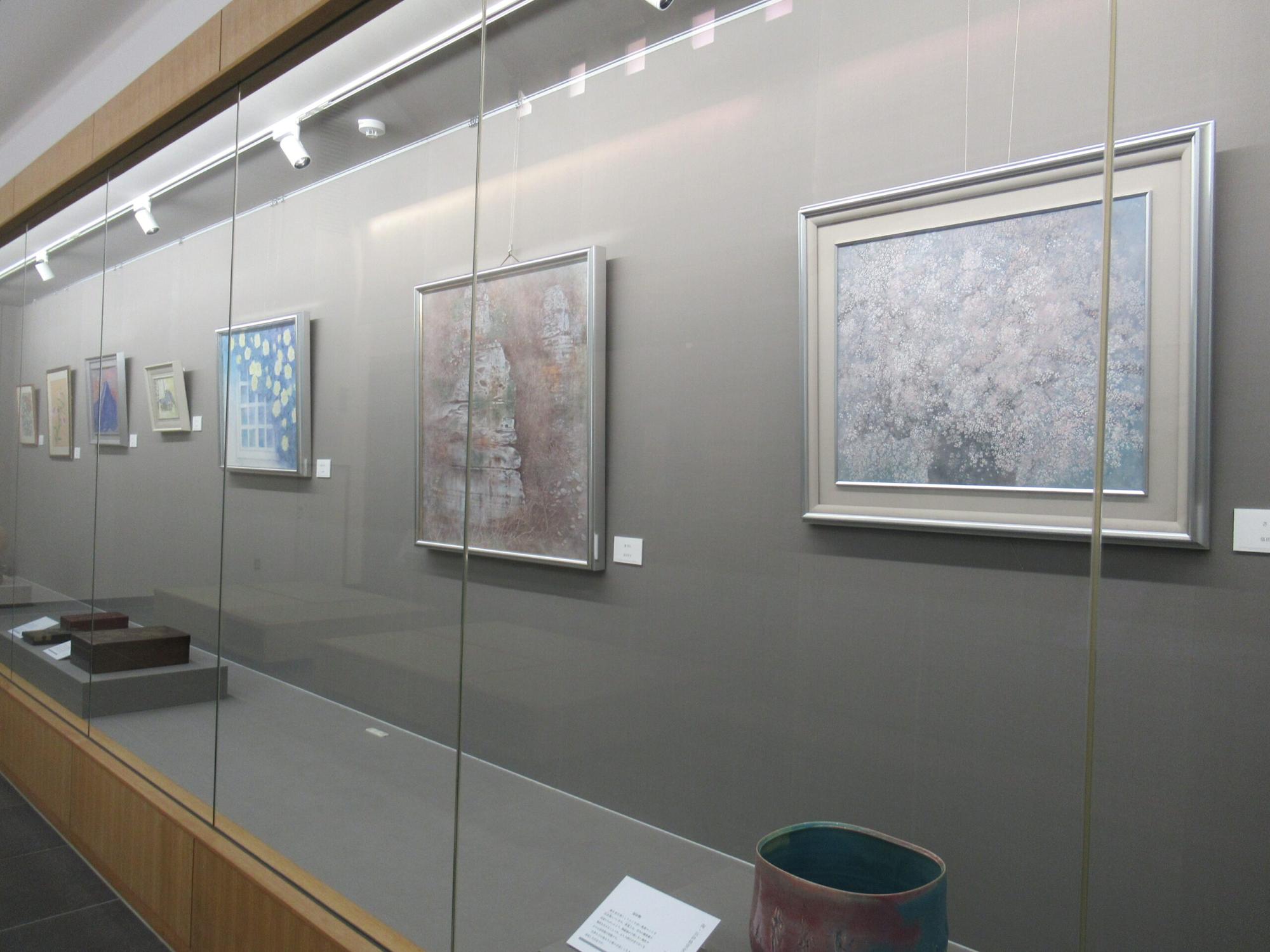 ガラス越しに並ぶ複数の絵画と陶器が落ち着いた照明の展示室に整然と配置され、静謐な雰囲気を静かに漂わせる写真