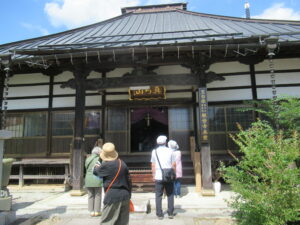 木造の大きな本殿前で数人が参拝をしている様子を捉えた写真