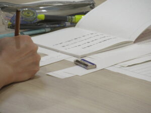 俳句が書き込まれたノートを広げ、短冊に俳句を記入している手元の写真