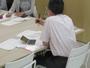 資料を広げたテーブルに座った参加者へ、選評をする佐藤健則先生の後ろ姿の写真