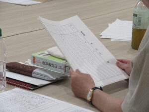 資料が置かれた机の前に座った人物が、選句用紙を手に持っている写真
