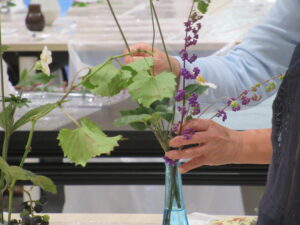 水色のガラスの花瓶に、紫の実をつけた枝や大きな葉を差し込みながら生けている手元の写真