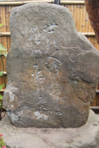 竹垣を背に丸みを帯びた石碑が据えられ白く刻まれた文字が風雨に磨かれた質感の中に浮かぶ写真