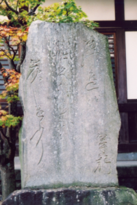 苔むした石碑が木々の葉を背景に堂々と立ち淡い刻字がしっとりと浮かび上がる情景の写真