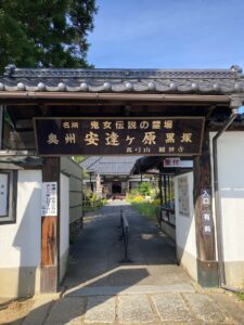 木造の門に「奥州安達ヶ原黒塚」の看板が掲げられた入口から、参道が奥の建物へ続く様子を映した写真