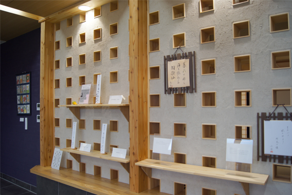 木枠に囲まれた多数の小さな四角い開口部を持つ壁に棚が設けられ、書やカード類が丁寧に展示されている写真