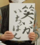 両手で「笑いがいちばん」と毛筆で書いた半紙を掲げている写真