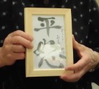 胸の前に掲げられた、書の作品が入った小さな木枠の額縁の写真