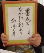 毛筆で書かれた俳句が入った木の額縁を両手で持っている写真