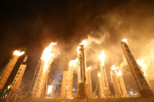 夜空を背に巨大な松明が林立し激しく燃え上がる炎と立ちこめる煙が迫力ある祭りの熱気を伝える写真
