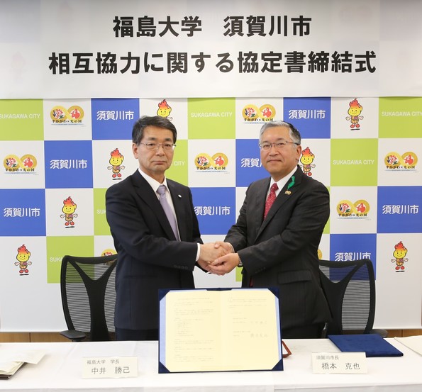 福島大学須賀川市相互協力に関する協定書締結式と書かれた横断幕を背景に、中井勝己福島大学学長と橋本市長が両手で握手を交わして記念撮影を行っている様子の写真