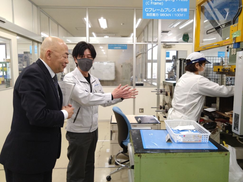 会議室で複数の参加者がコの字型に設置された長机に着席し、ノートパソコンや資料を前にプロジェクターで表示されたIT機器の管理ソリューションに関するスライドを見ながら説明を受けている様子の写真